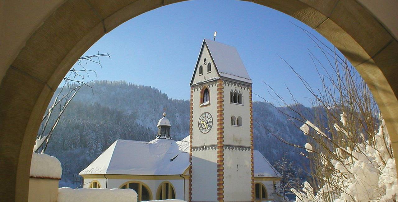 Entdecken Sie den verschneiten Kirchturm der Kirche St. Mang in Füssen im Allgäu.